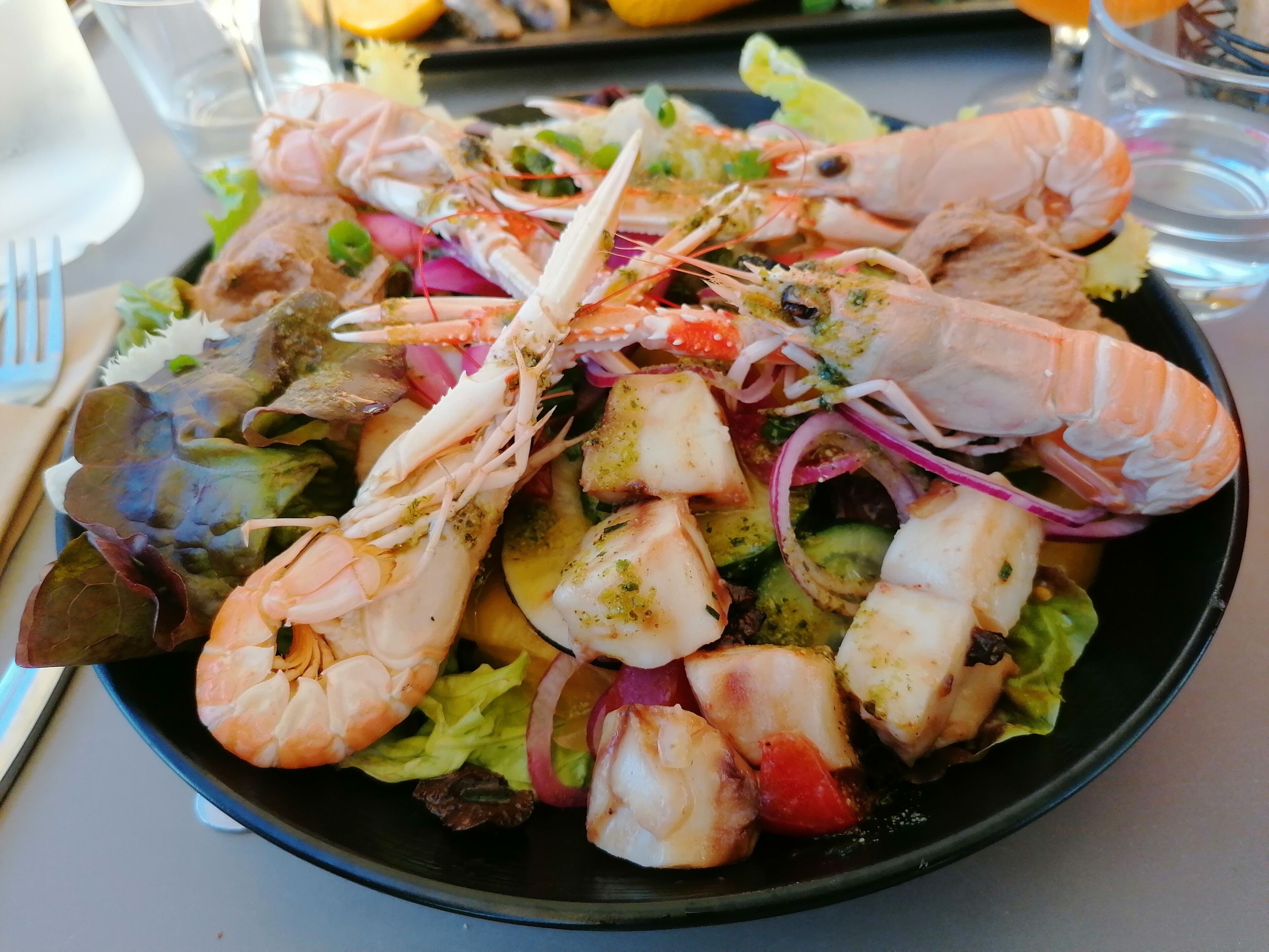 Une salade de fruits de mer composée de crevettes, de poisson et de légumes, servie dans une assiette noire.