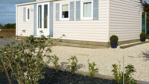 Een klein, gelijkvloers huis met schuine daklijn, witte bekleding en blauwe luiken.