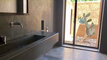 Une salle de bain moderne avec une grande baignoire, un lavabo et une douche. Une fenêtre offre une vue sur un cactus à l’extérieur.