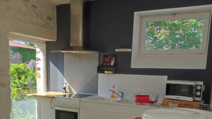 Cocina moderna con armarios blancos, encimera de madera, horno empotrado, microondas y ventana con vistas a la vegetación.