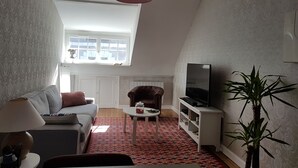 A living room with a sofa, a coffee table, a TV stand, a red hanging light, and a window with a view of the outside. - In the heart of the city center (Blois)