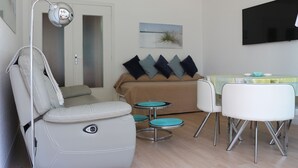 A modern living room with a sofa, a dining table with chairs, a small kitchen area, and a mounted TV. - Magnificent sea view in front of the beach at Trez de Bénodet (Bénodet)