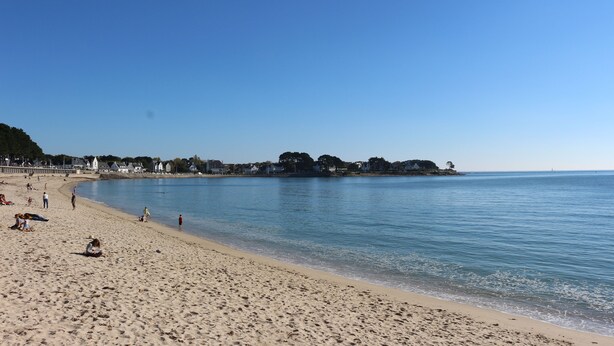 A wide sandy beach with clear blue water, a few people, and buildings in the background. - Magnificent sea view in front of the beach at Trez de Bénodet (Bénodet)