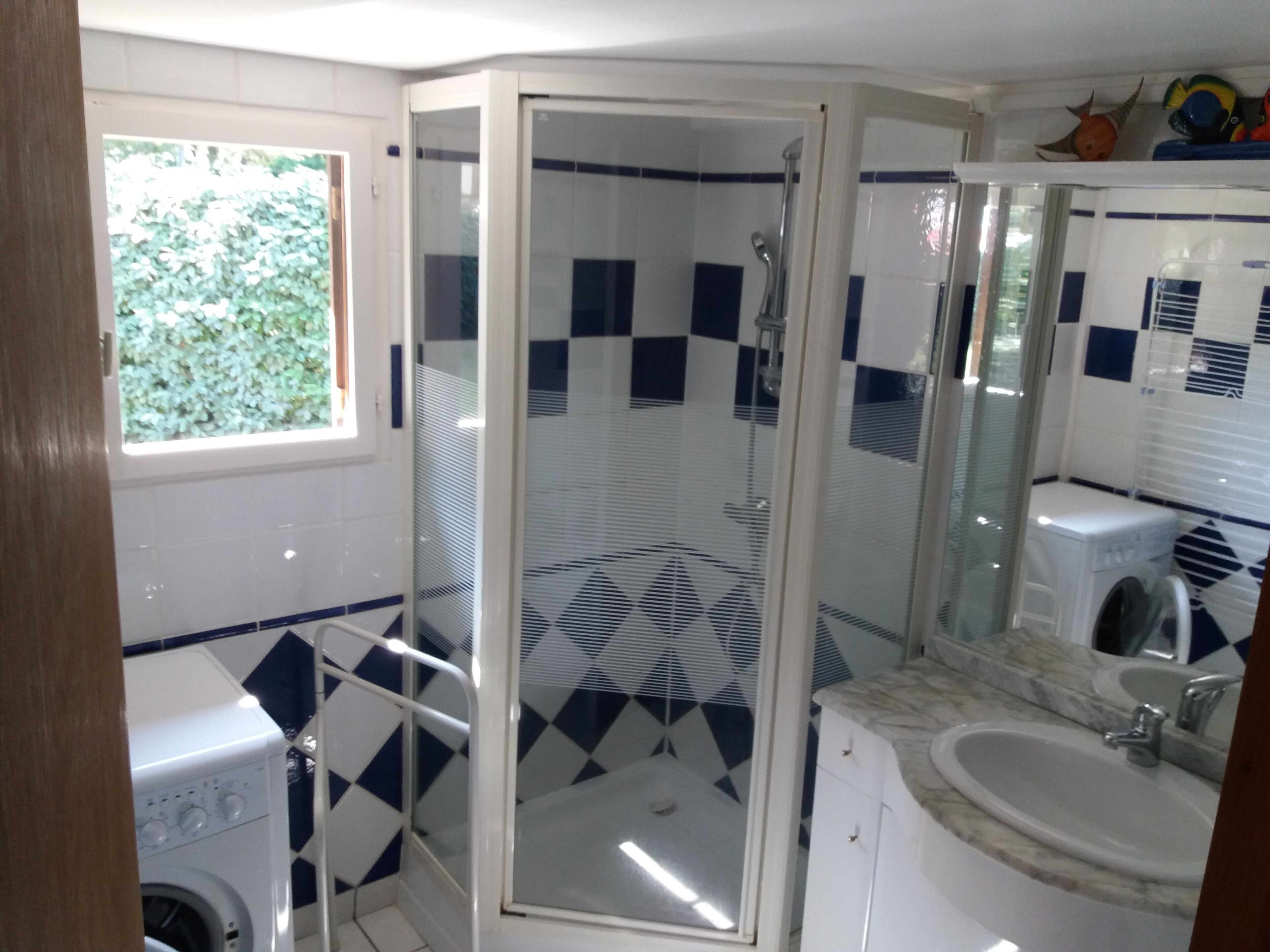 A bathroom with a glass-enclosed shower, a washing machine, and a sink with a mirror.