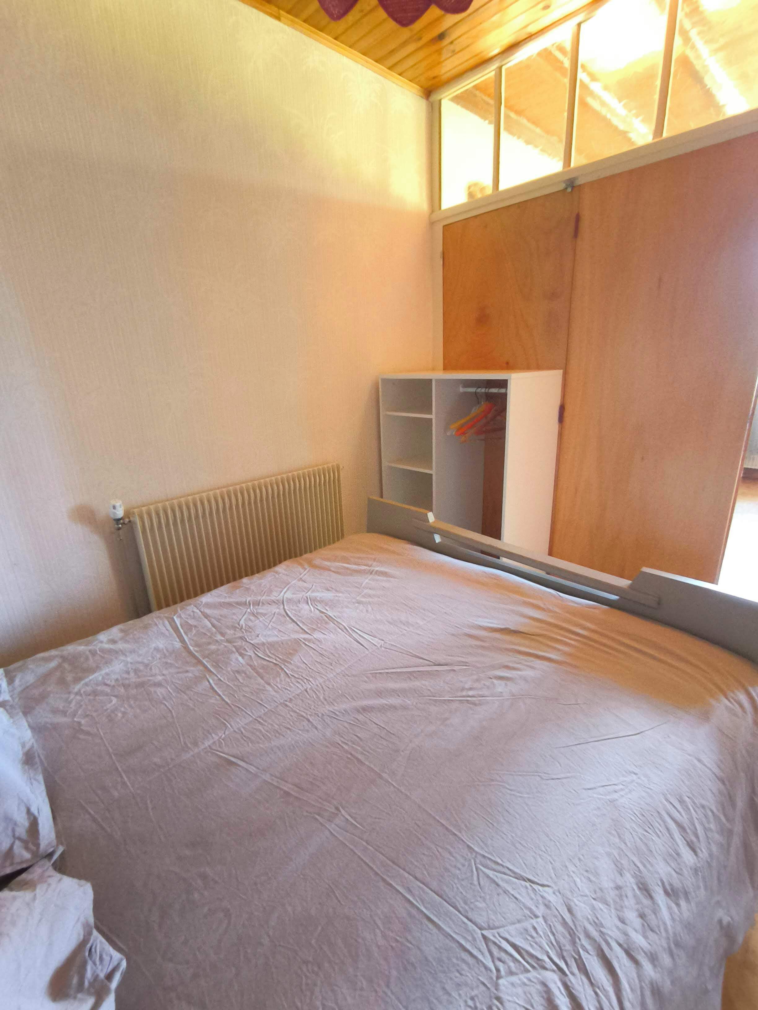 Een slaapkamer met een bed, een radiator, een houten kledingkast en een raam met uitzicht.