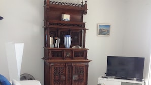 Una sala de estar con un sofá blanco, una mesa de centro de vidrio, un aparador de madera y un televisor.