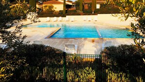 A swimming pool with white lounge chairs, surrounded by greenery and a fence. - MAZET DE LOLA little Provencal house (Saint-Rémy-de-Provence)