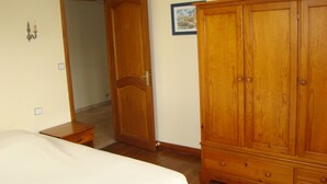 Un dormitorio con cama, armario de madera y una puerta que da a otra habitación.