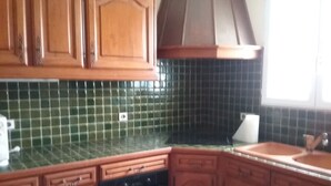 Una cocina con armarios de madera, horno negro y salpicadero de azulejos verdes.