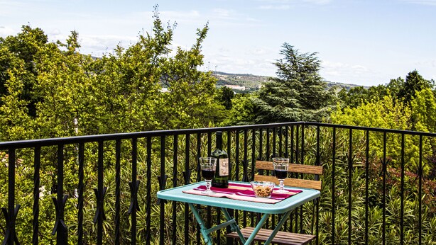 A balcony with a table set for two, a bottle of wine, and a bowl of snacks.