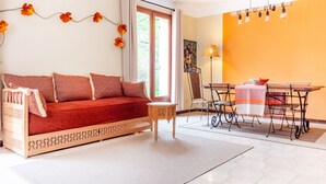 A cozy living room with a red sofa, a small wooden table, and a dining area with a table and chairs.