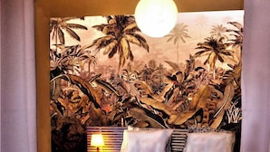 A bed with a tropical mural, a hanging light fixture, and a bedside lamp.