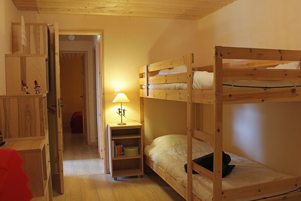A bunk bed room with a wooden desk and shelves, a lamp, and a door leading to another room.