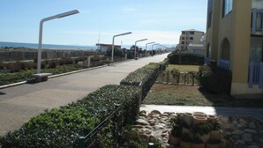 A paved walkway with street lamps, a grassy area with a low stone wall, and a building with balconies.