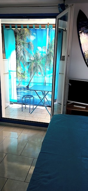 Une chambre dotée d’un lit, d’une télévision et offrant une vue sur une plage tropicale, avec des palmiers et une piscine.