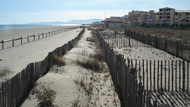 A beach with a wooden fence separating the sand from the buildings.