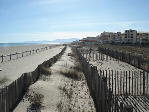 A beach with a wooden fence separating the sand from the buildings. - BARCARES. Res. the "Palm Beach" 50 meters from the Grande Plage. (Le BARCARES)