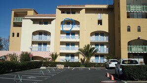 A multi-story hotel with balconies, a parking lot, and a clear blue sky.