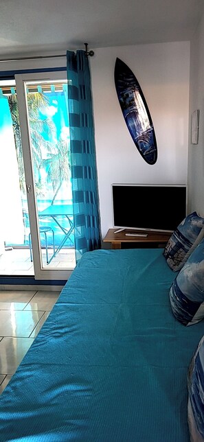 Una camera da letto con un letto, una TV, una decorazione a forma di tavola da surf e vista su palme attraverso la porta.
