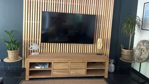 A modern living room with a large flat-screen TV mounted on a wooden slat wall, a wooden entertainment unit below, and a small side table with a decorative item. - Contemporary villa beach slope privileged site swimming pool (Capbreton)