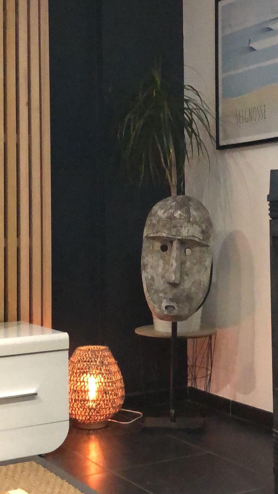 A room with a modern design, featuring a white cabinet, a decorative head sculpture, a potted plant, and a framed picture on the wall.