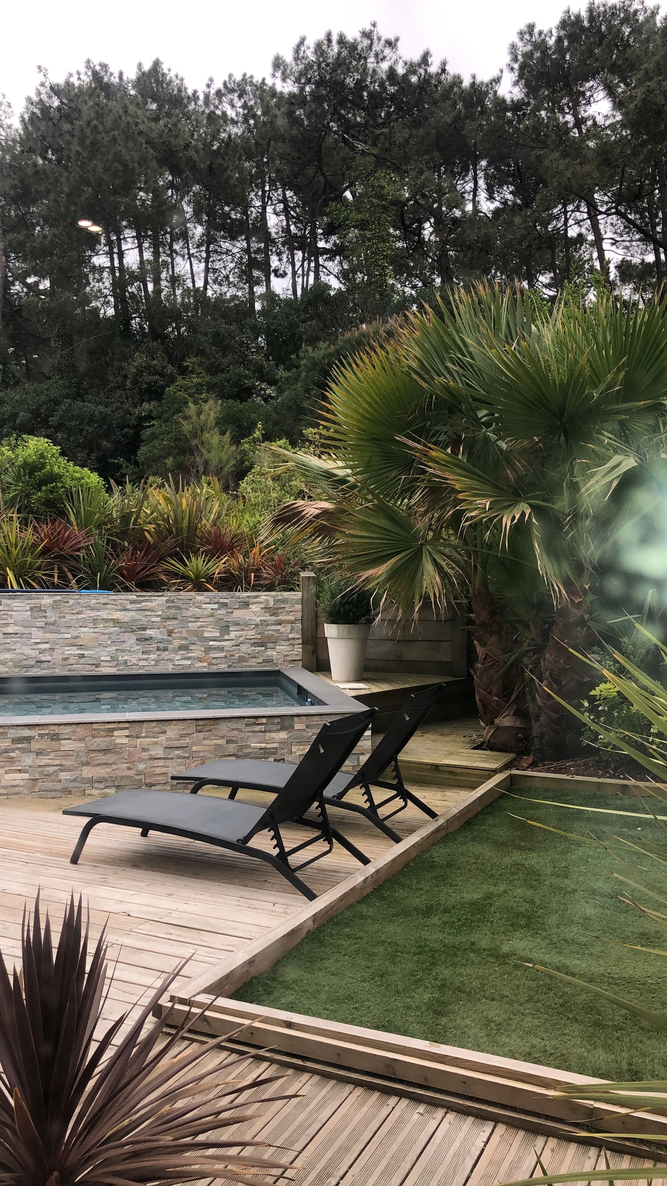 A poolside area with a stone wall, a small pool, and lounge chairs.