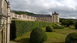 Un grand bâtiment historique doté d’un jardin à la française, avec des haies soigneusement taillées et une pelouse centrale.