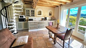 Une cuisine rustique avec un escalier en colimaçon, un coin repas avec une table et des chaises en bois, et une vue sur la verdure grâce à de grandes fenêtres.
