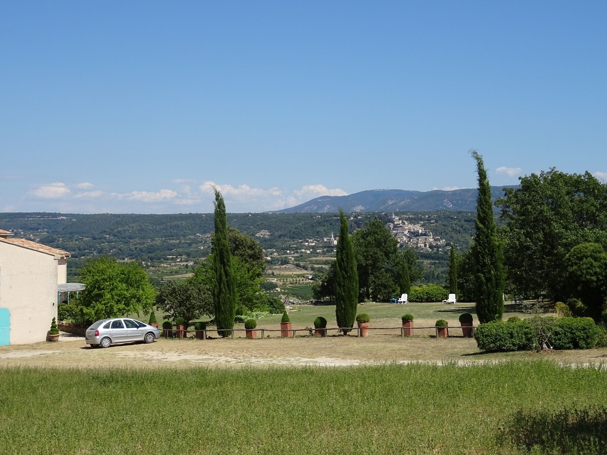 A rural landscape with a car parked in a driveway, surrounded by greenery and trees.