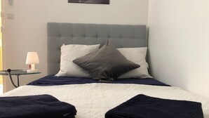 Uma cama bem arrumada com um edredom branco e duas toalhas azul-escuras dobradas no pé.