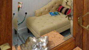 Um quarto com um sofá bege, uma moldura na parede e um espelho refletindo parte do ambiente.