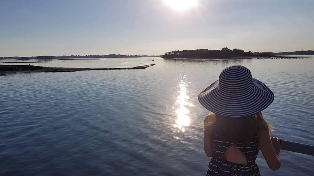 A person standing by a calm body of water with a distant shoreline.