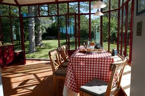 Ein Wintergarten mit kariertem Tischtuch, Holzstühlen und Blick auf den Garten.