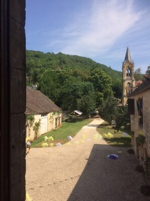 Un patio con un sendero de grava que conduce a una iglesia con campanario, rodeado de vegetación y edificios tradicionales.