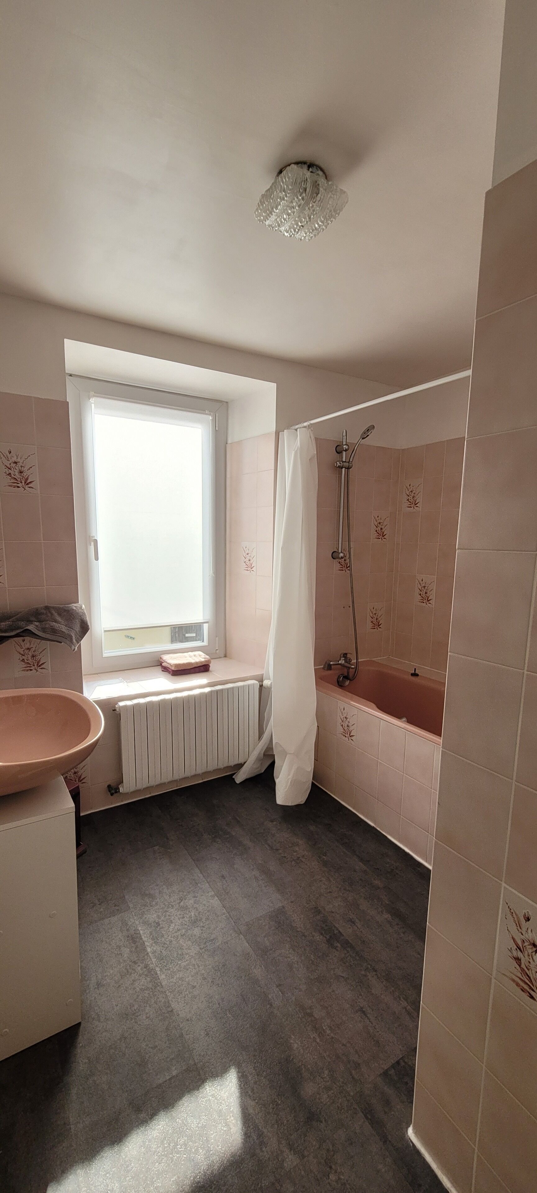 A bathroom with a window, a bathtub, a shower, a sink, and a radiator.