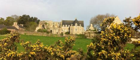 A historic stone building with multiple arches and a large lawn in the foreground.