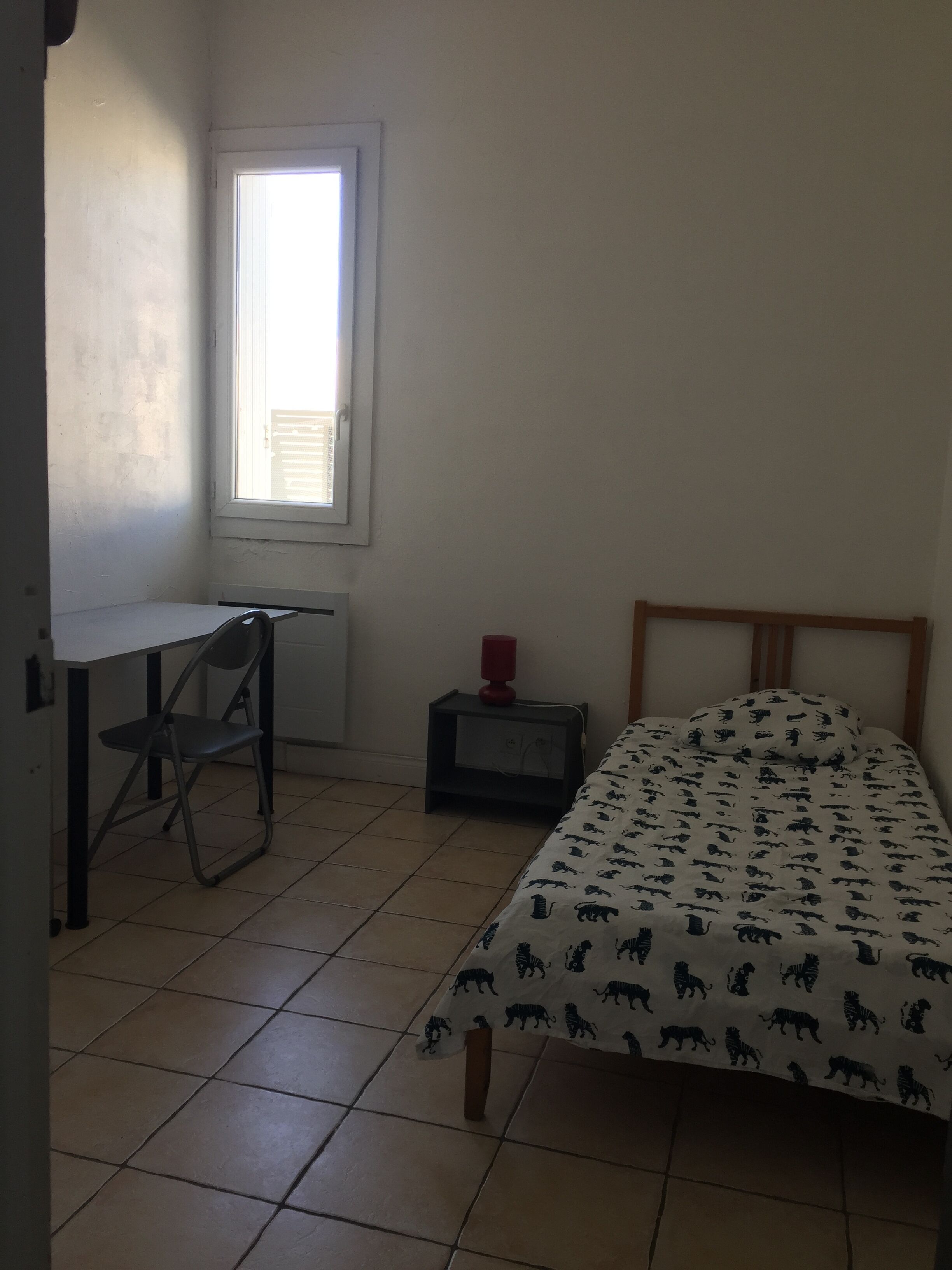 A bedroom with a bed, a desk, a chair, a nightstand, and a window.