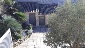 Un edificio de piedra con techo de tejas, un camino de piedra que lleva a una puerta y un gran árbol a la derecha.