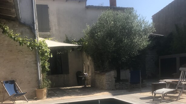 Una piscina cristalina con sillas de descanso y una mesa, rodeada de muros de piedra y vegetación.