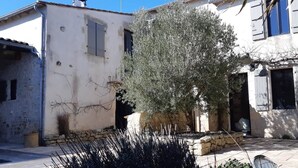 Un patio con muro de piedra, un árbol y un edificio con ventanas y contraventanas.