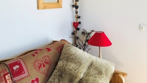 Un salón acogedor con un sofá, dos lámparas de pared rojas, un espejo de madera y una planta decorativa.