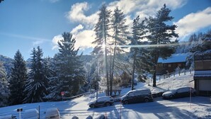 Un estacionamiento nevado con autos, un banco de madera y un edificio con techo cubierto de nieve.