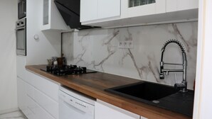 Una cocina con armarios blancos, salpicadero de mármol, encimera de madera, pileta negra y lavavajillas integrado.
