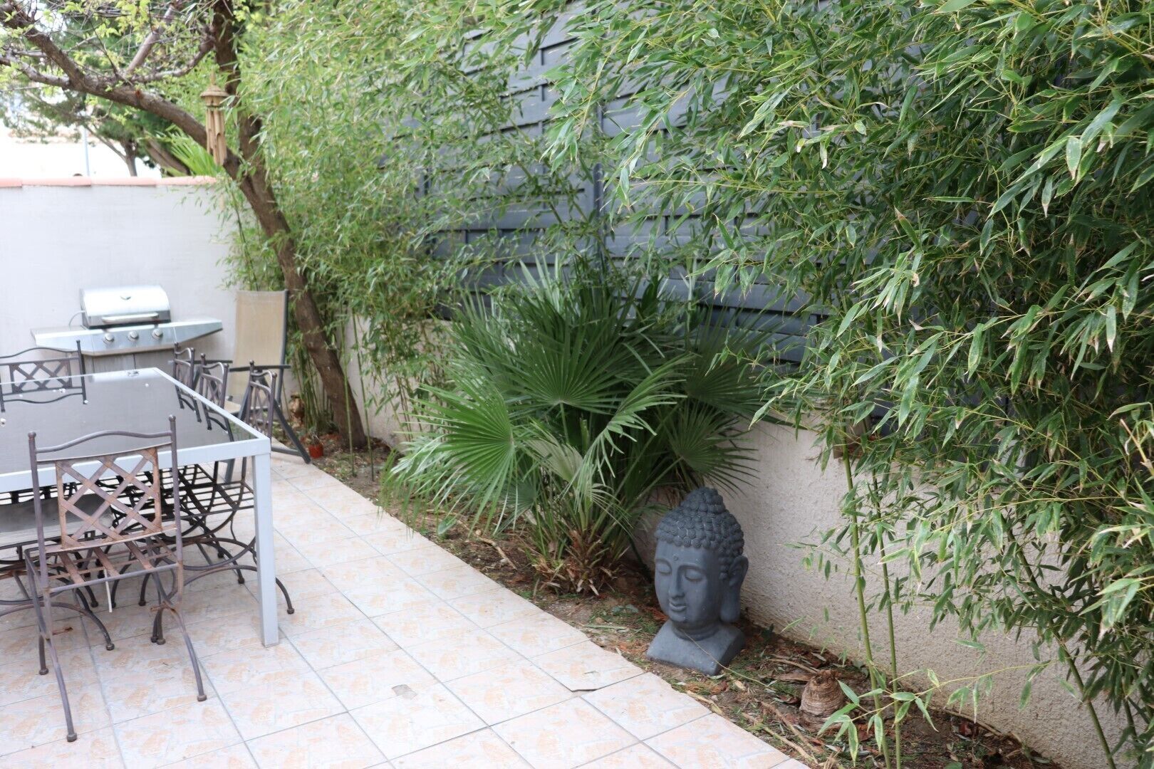En terrasse med bord og stole, en Buddha-statue og en væg dækket af vegetation.