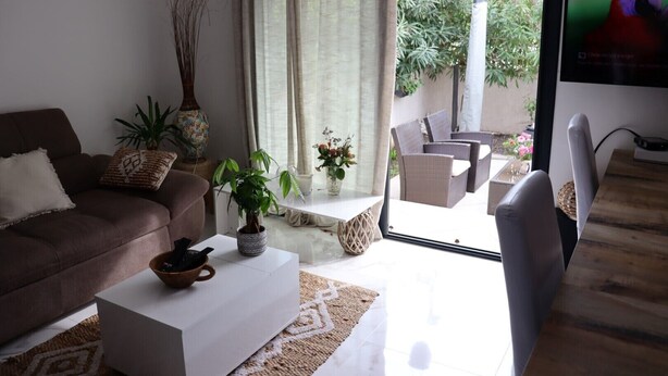 Un salón con un sofá marrón, una mesa de centro blanca y un televisor sobre un mueble de madera.