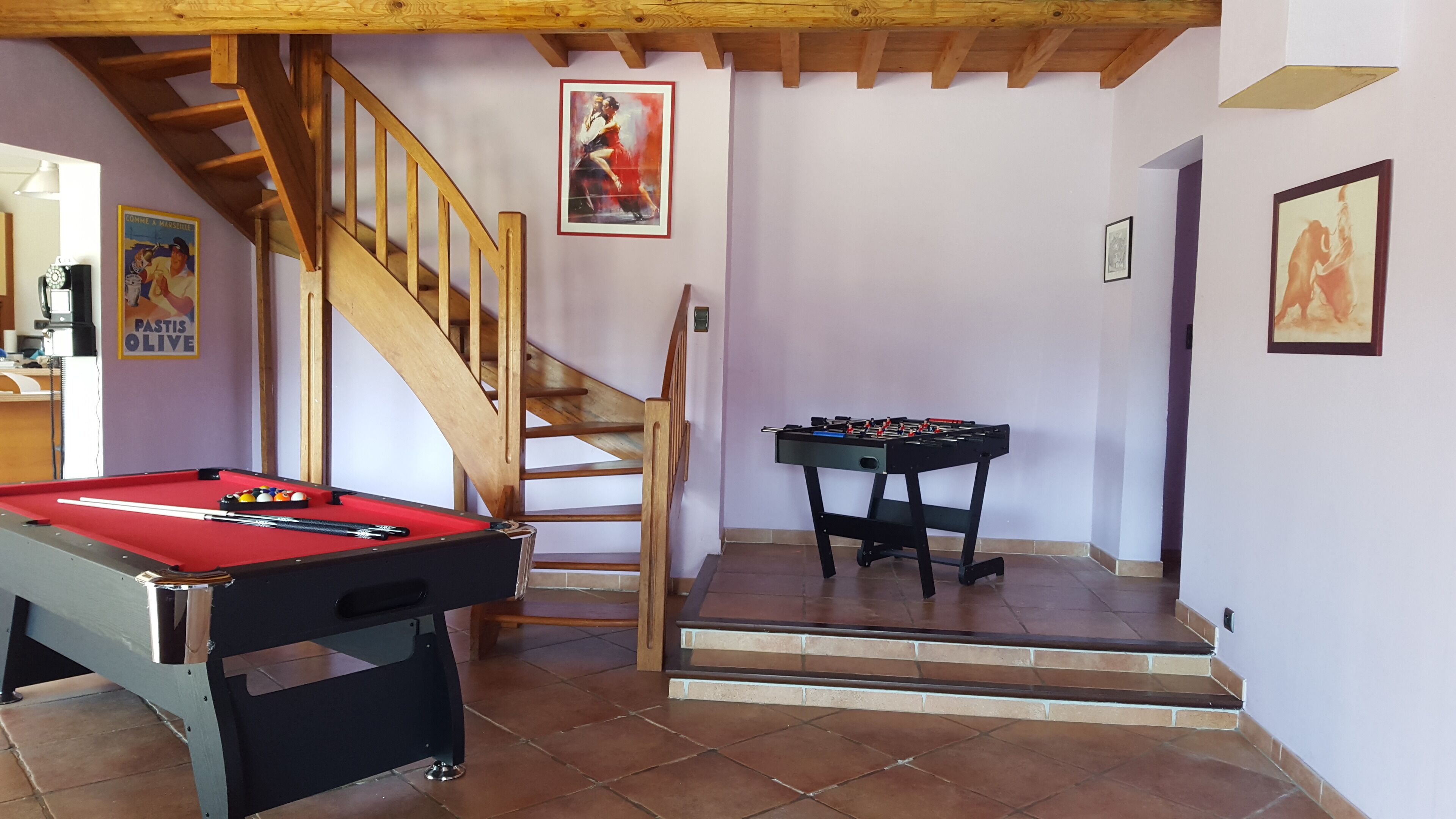 A room with a pool table, foosball table, and a wooden staircase.