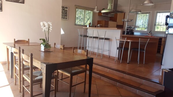 A modern kitchen with a wooden dining table, bar stools, and a staircase leading to a second floor.
