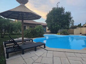 Piscina com espreguiçadeiras e um guarda-sol de palha.