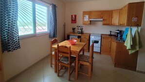 A compact kitchen with wooden cabinets, a stove, and a dining area with a table and chairs. - Accommodation for 2 people, swimming pool, bikes in Morro île de Maio (Morro)
