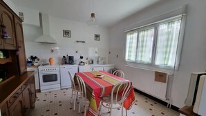 A compact kitchen with white appliances, a dining table with chairs, and a window with curtains. - Country house with wonderful view over the Lot valley (Galapian)